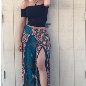 Puede incluir: Un top negro de hombros descubiertos con mangas cortas combinado con una falda larga de color verde azulado con un vibrante estampado floral y geométrico multicolor, cintura alta y una abertura lateral que llega al muslo.