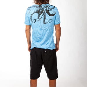May include: A light blue short-sleeve t-shirt featuring a large black octopus graphic printed across the upper back and shoulders, paired with black knee-length shorts that have a small black label on the back pocket area.