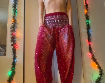 Può includere: Pantaloni rossi, bianchi e dorati con motivo a stampa e una cintura elastica larga. I pantaloni hanno una vestibilità ampia e fluida e sono raccolti alle caviglie.
