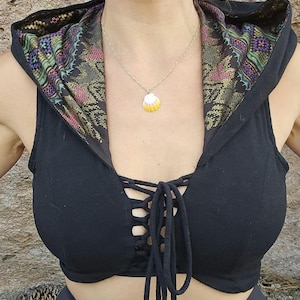 May include: A black sleeveless hooded crop top featuring a front lace-up closure with matching black ties. The interior of the hood is lined with a vibrant, multi-colored woven fabric pattern in shades of green, purple, and gold.