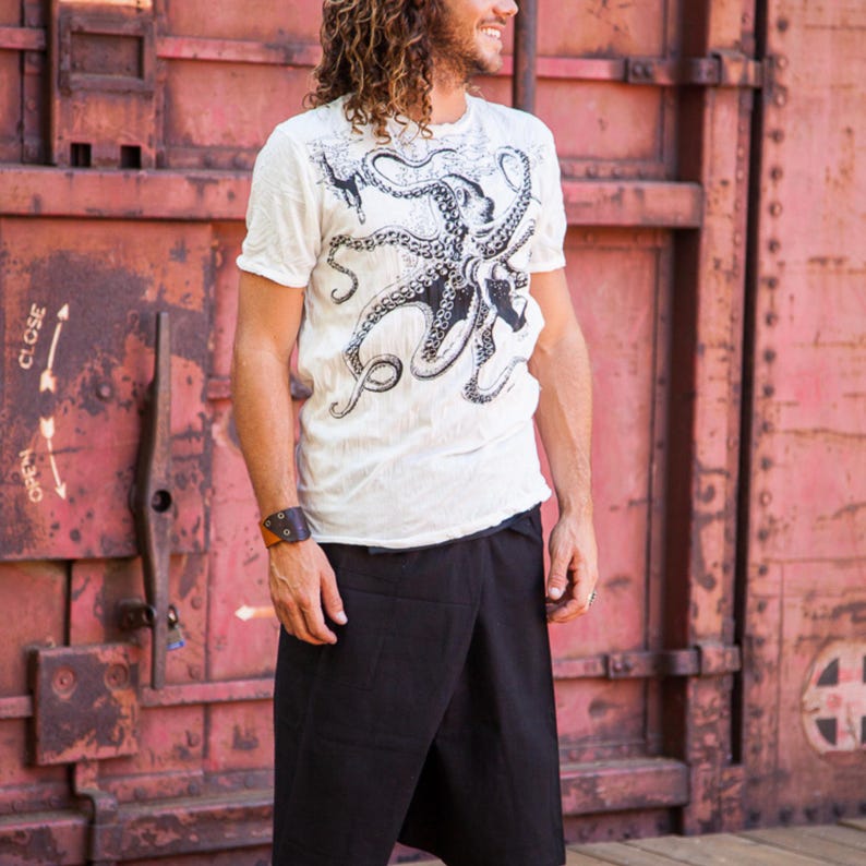 May include: A white short-sleeved t-shirt featuring a large black octopus graphic on the front, paired with black wrap-style shorts. The t-shirt has a crew neckline and the octopus design covers the chest area with detailed tentacles and suckers.