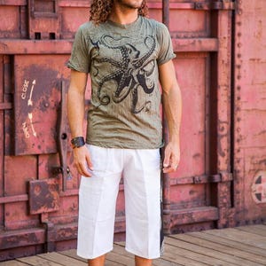 May include: An olive green short-sleeve t-shirt featuring a large black octopus graphic on the chest, paired with white knee-length shorts that have a black vertical side panel with a patterned design along the outer leg seam.