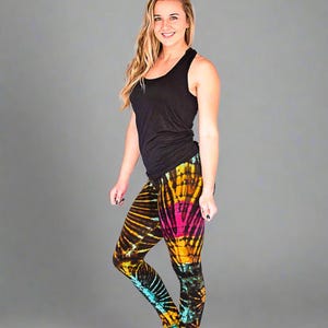 May include: A woman wearing a black tank top and colorful tie-dye leggings. The leggings have a bright yellow, pink, blue, and black pattern.