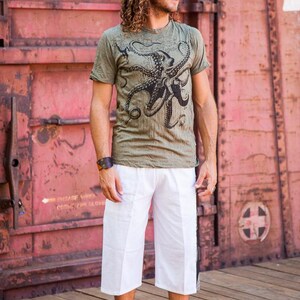 May include: An olive green short-sleeved t-shirt featuring a large black octopus graphic print on the front, paired with loose-fitting white knee-length shorts. The t-shirt has a crew neckline and the shorts have a straight-leg cut.