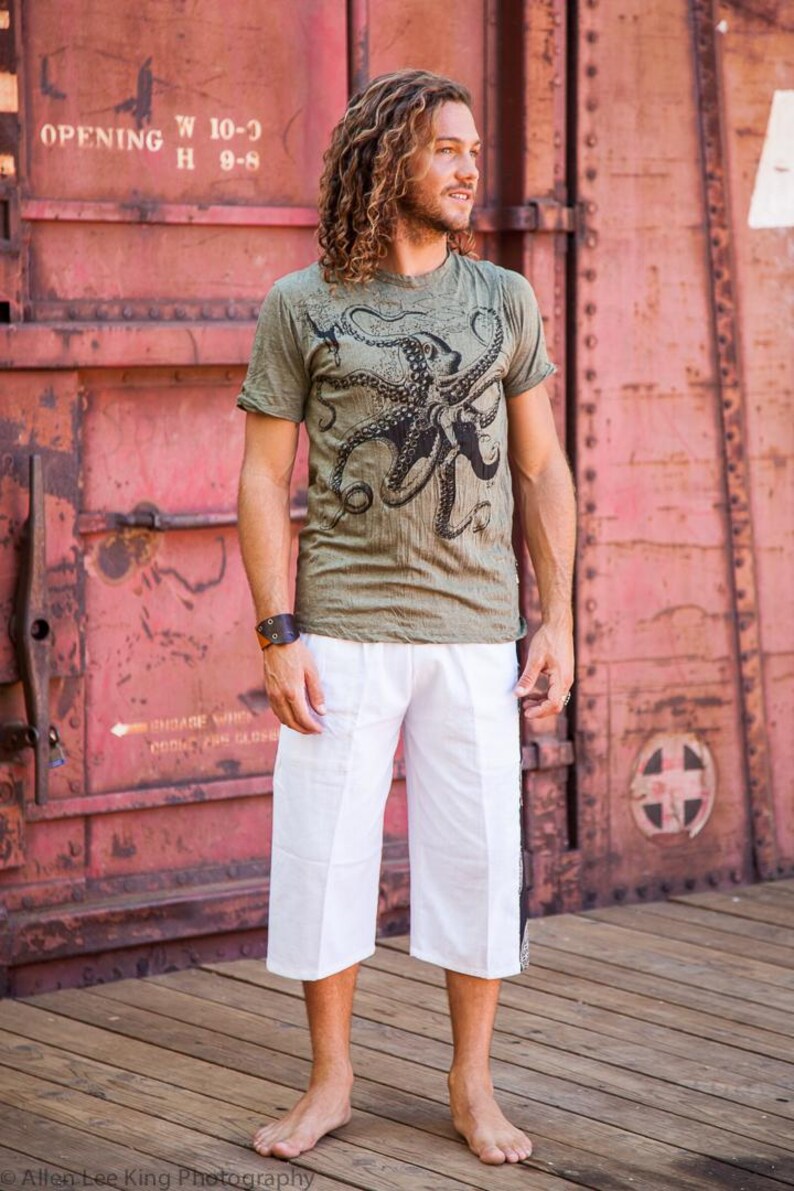 May include: An olive green short-sleeved t-shirt featuring a large black octopus graphic print on the front, paired with loose-fitting white knee-length shorts. The t-shirt has a crew neckline and the shorts have a straight-leg cut.
