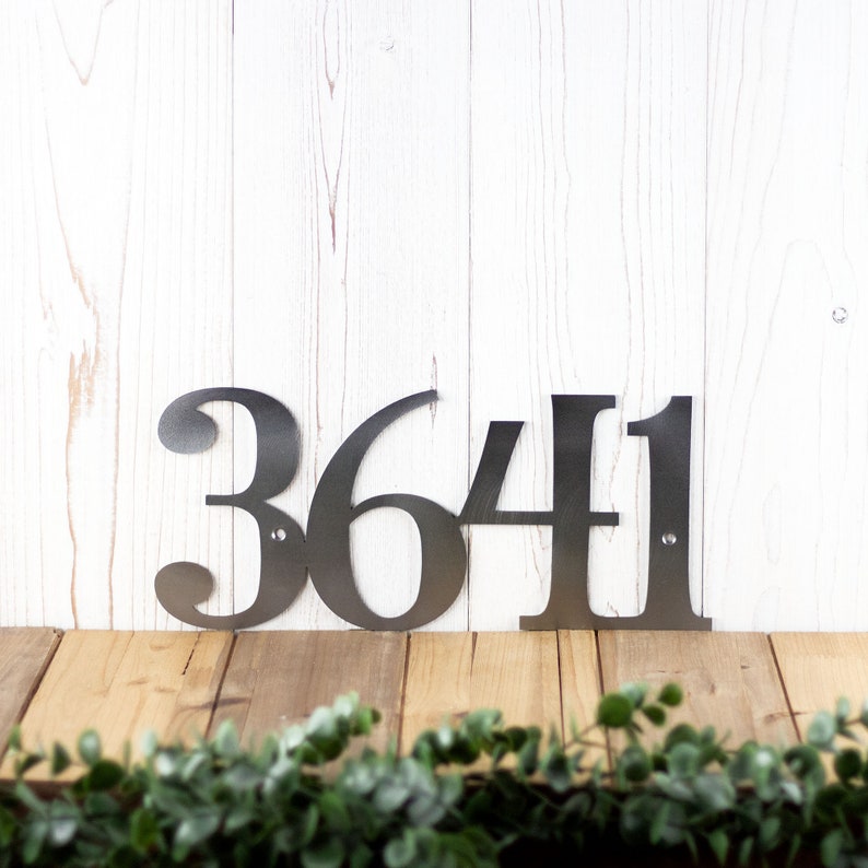 4 digit metal house number plaque, in raw steel. Placed against a wood wall.