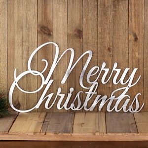 Merry Christmas script metal wall art, in raw steel. Placed against a wood wall.