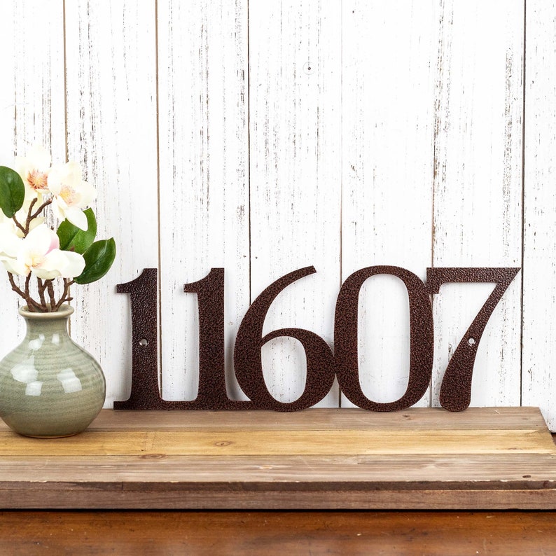 5 digit metal house number plaque, in copper vein powder coat. Placed against a white wood wall.