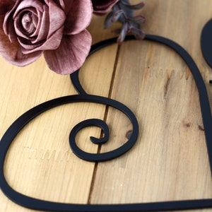 Close up of matte black powder coat on our God Bless our Home metal wall decor. Placed on a wood plank.