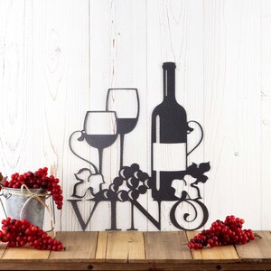 Vino metal wall art with wine glasses, bottle, and grapes, in silver vein powder coat. Placed against a white wood wall.
