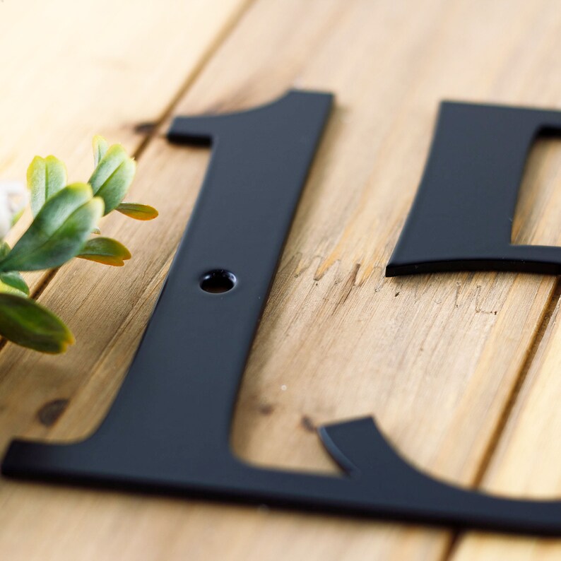 Close up of matte black powder coat on our metal address sign. Placed on a wood plank.