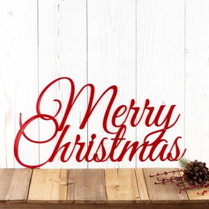 Merry Christmas script metal sign, in red gloss powder coat. Placed against a white wood wall.