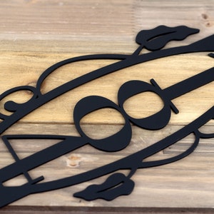 Close up of 3 digit house number on our vertical metal address sign, in matte black powder coat. Placed on a wood plank.