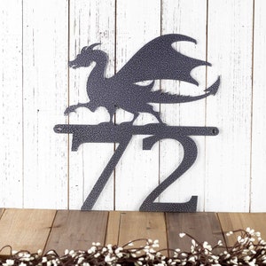 2 digit metal house number sign with a dragon silhouette, in silver vein powder coat. Placed against a white wood wall.
