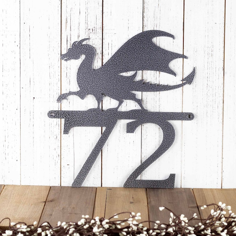 2 digit metal house number sign with a dragon silhouette, in silver vein powder coat. Placed against a white wood wall.