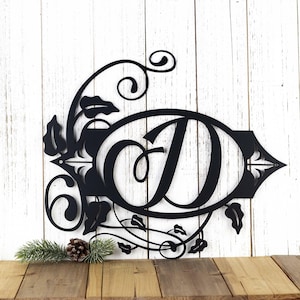 May include: Black metal monogram with a decorative floral design and the letter "D" in a cursive font.