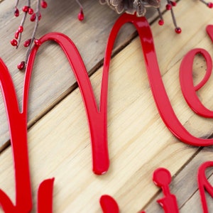 Close up of red gloss powder coat on our script Merry Christmas metal wall art. Placed on a wood plank.