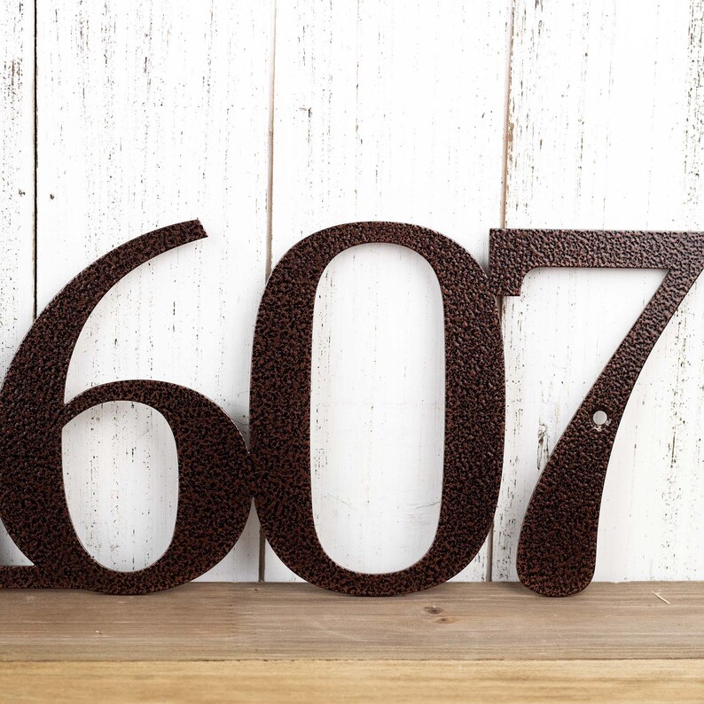 Close up of house number on our metal address sign, in copper vein powder coat. Placed against a white wood wall.