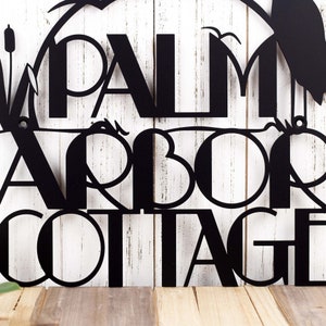 Art deco metal house name plaque with heron and cattails lake scene, in matte black powder coat.