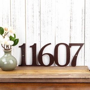 5 digit metal house number sign, in copper vein powder coat. Placed against a white wood wall.