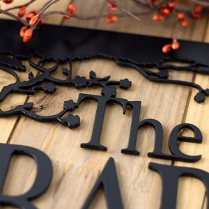 Close up of matte black powder coat on the metal family name sign. Placed on a wood plank.