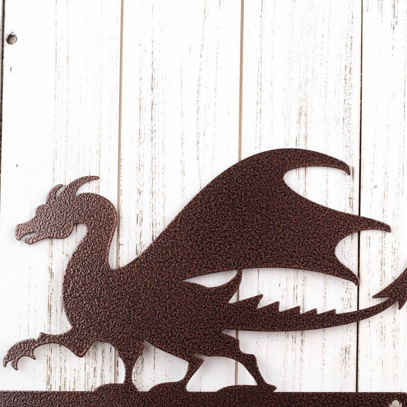 Close up of dragon silhouette on our metal address sign, in copper vein powder coat. Placed against a white wood wall.