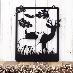 May include: Black metal wall decor featuring a silhouette of two deer in a forest setting. The deer are standing side-by-side, with leaves and branches in the background.