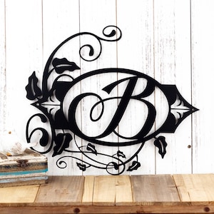 May include: Black metal monogram with a decorative floral design and the letter "B" in a cursive font.
