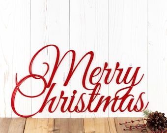May include: Red metal "Merry Christmas" sign with a pine cone and red berries on a wooden surface.