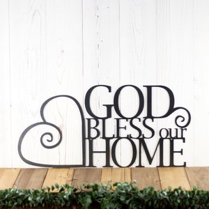 God Bless our Home metal sign with heart, in silver vein powder coat. Placed against a white wood wall.
