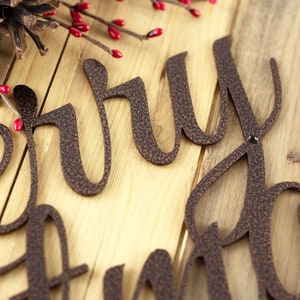 Close up of copper vein powder coat on our script Merry Christmas metal plaque. Placed on a wood plank.