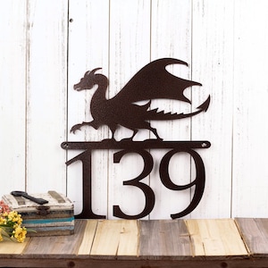 3 digit metal house number sign with a dragon silhouette, in copper vein powder coat. Placed against a white wood wall.