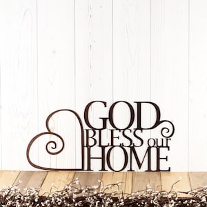 God Bless our Home metal wall decor with heart, in copper vein powder coat. Placed against a white wood wall.