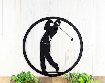 May include: A black circular metal wall art piece featuring a silhouette of a golfer in a mid-swing position. The golfer is wearing a cap and holding a golf club extended upwards. The design is contained within a solid black circular frame.