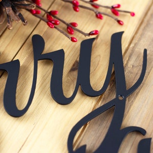 Close up of matte black gloss powder coat on our script Merry Christmas metal wall art. Placed on a wood plank.