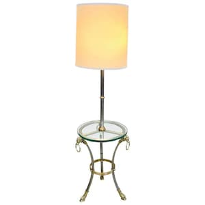 May include: A silver and brass floor lamp with a white drum shade and a glass top table. The table has three legs with brass lion paw feet.