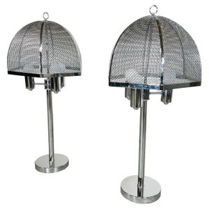 May include: Two chrome table lamps. Each lamp has a dome-shaped, mesh shade with a ring at the top. The lamps have a cylindrical base and stem. The lamps are a modern design.