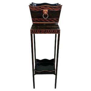 May include: Black and gold decorative plant stand with a rectangular top and a lower shelf. The stand features a lion's head with a ring handle and decorative trim. The stand is approximately 40 inches tall.