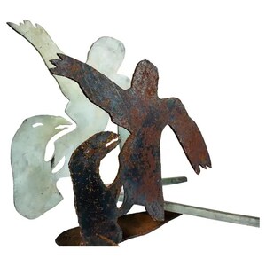 May include: A metal sculpture of three figures, two standing and one lying down. The figures are made of rusted metal and are silhouetted against a white background.