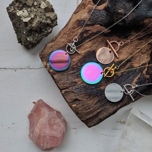 Può includere: Quattro collane con ciondoli rotondi iridescenti su una superficie di legno. Le collane hanno catene e chiusure a levetta di diversi colori.