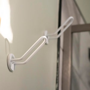 May include: Two white, metal hooks with a suction cup base mounted on a white wall. The hooks are designed to hold items like towels or robes.