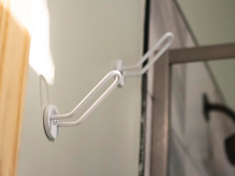 May include: Two white, metal hooks with a suction cup base mounted on a white wall. The hooks are designed to hold items like towels or robes.