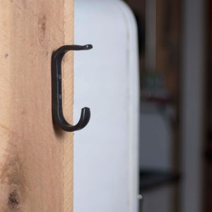 May include: A black metal hook mounted on a wooden surface.