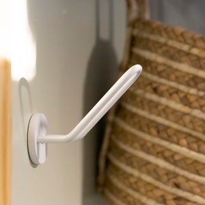 K&ouml;nnte beinhalten: Wei&szlig;er Saugnapfhaken mit einem gebogenen Arm, montiert an einer wei&szlig;en Wand. Der Haken ist so konzipiert, dass er Gegenst&auml;nde wie Handt&uuml;cher oder Badem&auml;ntel h&auml;lt.