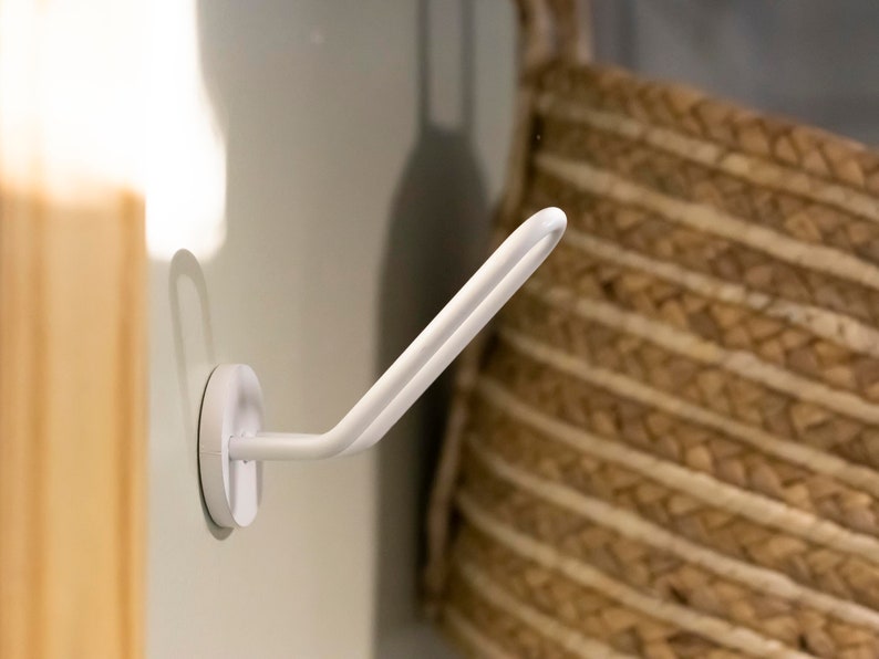 K&ouml;nnte beinhalten: Wei&szlig;er Saugnapfhaken mit einem gebogenen Arm, montiert an einer wei&szlig;en Wand. Der Haken ist so konzipiert, dass er Gegenst&auml;nde wie Handt&uuml;cher oder Badem&auml;ntel h&auml;lt.