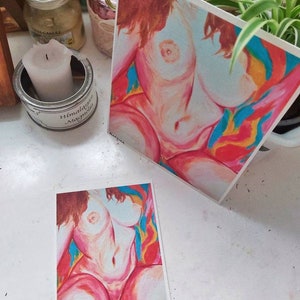 May include: Two prints of a nude female figure in a colorful abstract background. The figure is painted in a realistic style with soft pink and white tones. The background is a vibrant mix of red, orange, yellow, blue, and green.