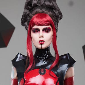 May include: A glossy red and black latex garment featuring a high collar, structured shoulder details, and a central black circular emblem. The outfit includes matching red latex arm sleeves and a belt with a silver buckle, worn with red hair.