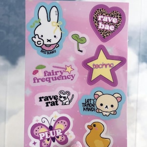 May include: A sheet of stickers with a pink background featuring various cartoon designs and text. Designs include a bunny, heart with leopard print, star, mouse, butterfly, duck, and text that says "rave bae", "techno", "fairy frequency", "rave rat", "Let's Trade Kandi", and "PLUR".