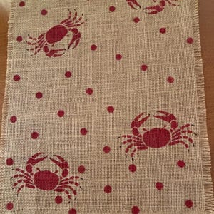 Puede incluir: Un camino de mesa de arpillera con un patrón de lunares rojos y blancos y siluetas de cangrejos rojos.