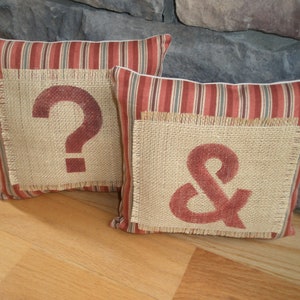 May include: Two decorative throw pillows with red and white striped fabric and burlap patches. The burlap patches have a red question mark and ampersand.